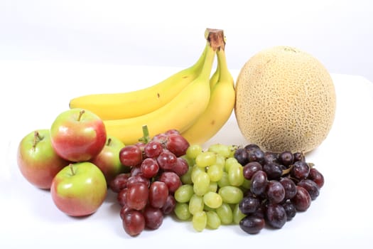 Colorful fresh fruits like grapes, cantaloupe,apples,and bananas on a white background