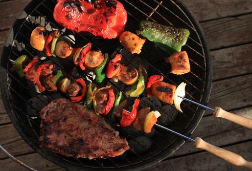 Barbecuing shish kabobs with sausage, steak and peppers, in green and red on a portable charcoal bbq