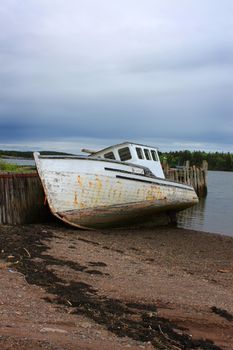 Beached fishing boat leaning against a wooden pier under dark sky in the Bay of Fund,  Maces Bay, New Brunswick, Canada