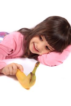 Young little girl laying on white background holding a banana and smiling