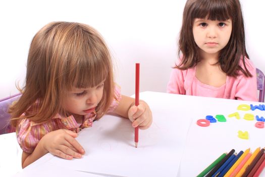 Two little preschool girls, one drawing with pencil the other playing with letters