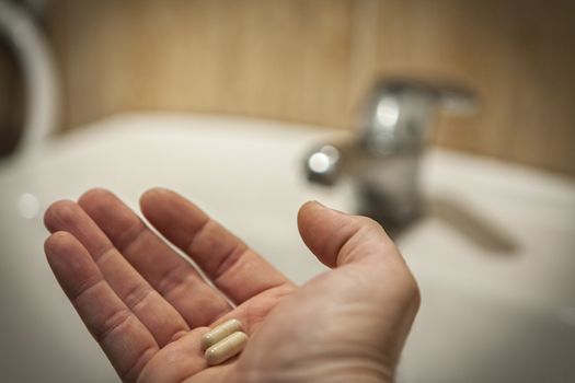 middle-aged man's hand holding two blue pills in bathroom scene 