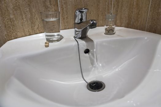 Glass of water and pile of blister packs in bathroom shelf