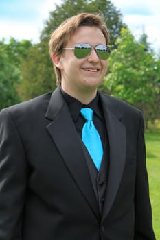 Handsome, smiling young man wearing a formal suit and mirror glasses going to the prom or a groom at a wedding