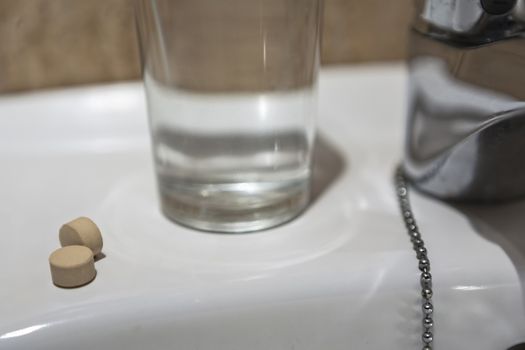 Glass of water and pile of blister packs in bathroom shelf