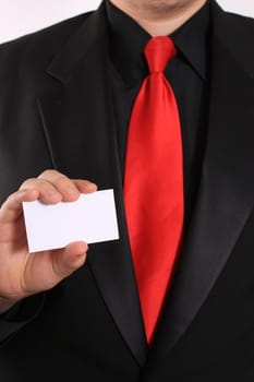 Businessman holding a blank business card in one hand showing his black suit and red tie (focus on card)