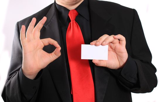 Businessman holding a blank business card in one hand and making an ok gesture in the other on a white background (focus on card)