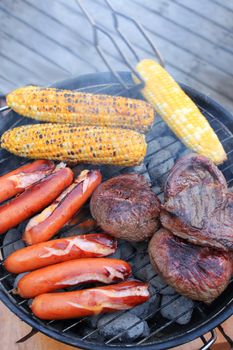 Smokey barbecue cooking on coals in the great outdoors consising of corn on the cob, round steak, and sausages