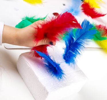 Little girls hands playing with colorful feathers, creating Easter decoration