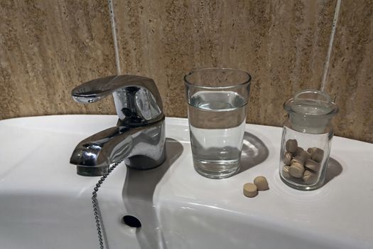 Glass of water and pile of blister packs in bathroom shelf