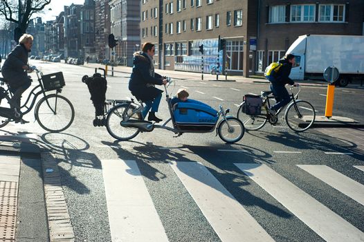 AMSTERDAM, NETHERLANDS - FEB 26, 2014: Unidentified people  crossing the street by bicycle. It is one of the most cycle-friendly cities in the world. 58% of the citizens uses daily a bicycle.