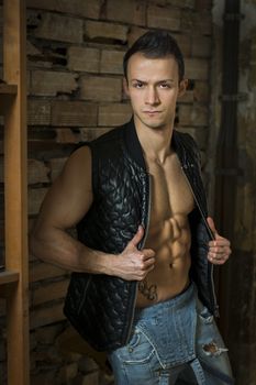 Muscular shirtless young man with jeans, indoors. Old brick wall behind. Looking at camera