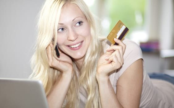 Smiling young woman using laptop, holding golden credit card