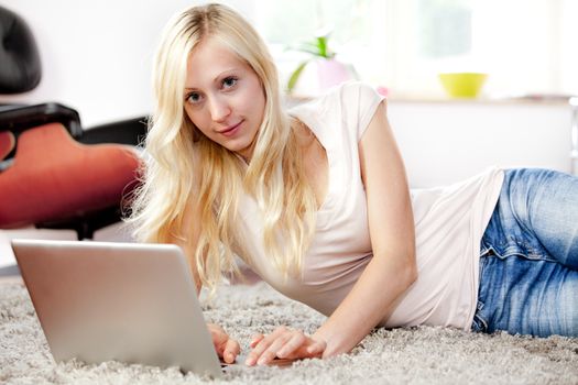 Releyed woman is using the laptop in her livingroom, lying on the carpet