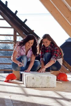 Two young women workers sitting on under construction roof, and control building in accordance with drawing