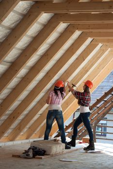 Two young long-haired woman hammered nails into a wooden construction of a new roof on the house