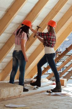 Two young long-haired woman hammered nails into a wooden construction of a new roof on the house