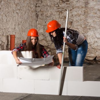 Two young long-haired woman repairing the old house and build a new wall from blocks in accordance with drawing