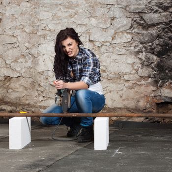 Young long-haired woman cut iron pipe with angle grinder during the repair an old house