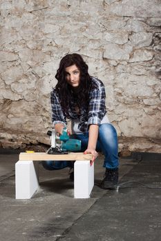 Young long-haired woman with a circular saw cuts wood at repair of an old house