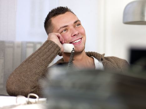 Smiling young businessman having conversation on landline phone. Horizontal shot