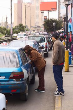 LIMA, PERU - JULY 21, 2013: Unidentified woman asking a taxi for the fare in front of the mall Polvos Azules on Av. Paseo de la Republica in the city center on July 21, 2013 in Lima, Peru. In Lima, taxi fares are agreed upon beforehand, fares are not standardized.