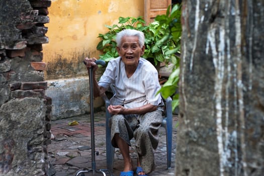 HOI AN, VIET NAM- MAY 13: The old lady sitting on chair with crutch on hand at gateway's house, Hoi An, May 13, 2012