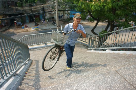 SAI GON, VIET NAM- APRIL 8: Old men carrying bicycle by hand go up to stair, he is accross the waterway on overpass in Sai gon, Viet Nam, April 8, 2013