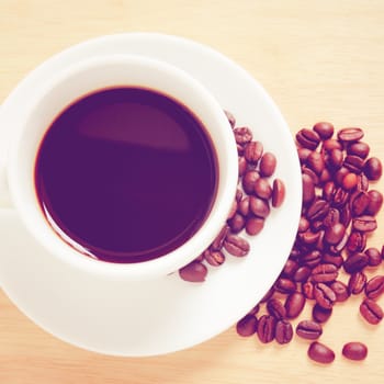 Coffee cup and beans on wooden table with retro filter effect