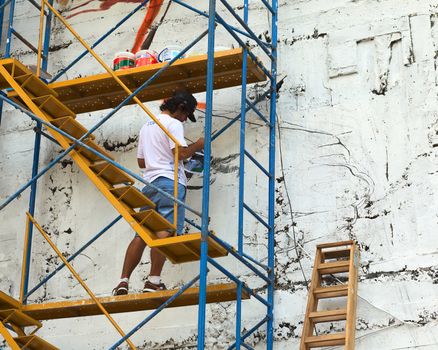 LIMA, PERU - MARCH 3, 2012: Unidentified young man painting a high outside wall of a building standing on a scaffold on March 3, 2012 in Miraflores, Lima, Peru