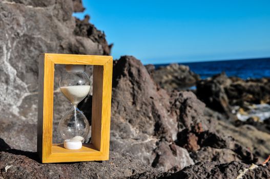 Time Concept White Sand Hourglass on the Volcanic Rocks