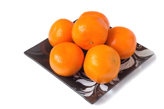Large ripe oranges are located on a dish made of dark glass with ornament. Presented on a white background