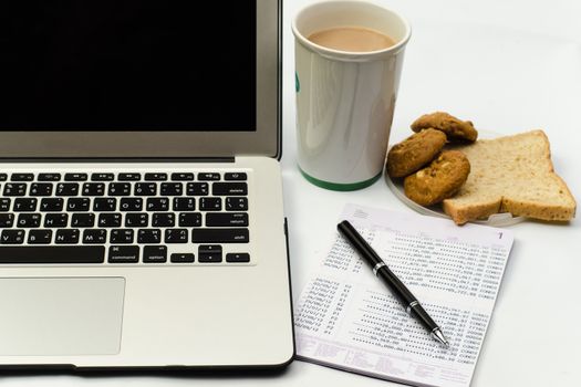 Office desk with laptop, book bank,cookie bread and cup of coffee