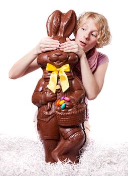 Blond Girl Hiding the eyes of a Chocolate Bunny Isolated on white background