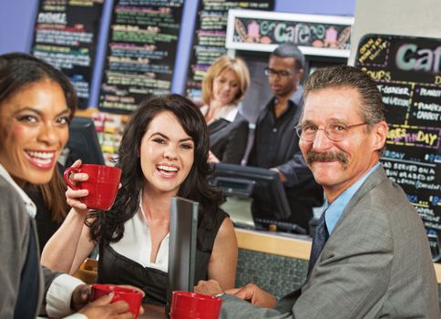 Three business people smiling as they drink in cafe