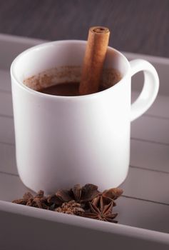 Hot chocolate with stick of cinnamon and star anise over wooden background