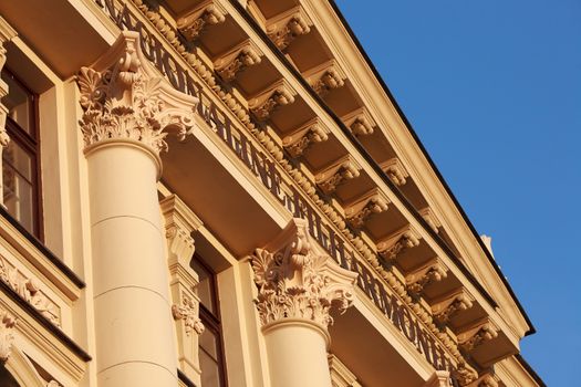 Fragment of classic or neoclassic building with columns and fine capitals, illuminated with warm summer sunlight, blue sky visible.