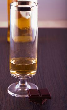 Blocks of chocolate near a long glass of whisky, with a bottle on the back