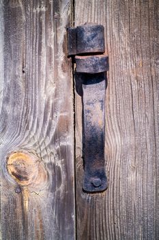 Old, wrought, damaged, rust hinge in old wooden door, illuminated by sunlight.