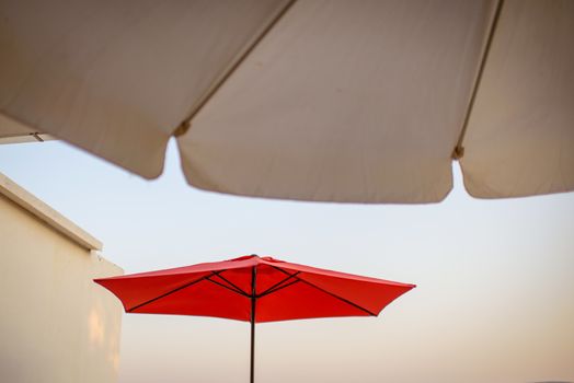 Two terrace, garden umbrella, red and white,  against blue sea and cloudless sky, visible coastline, ship in distance.