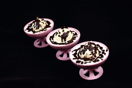 On a black background are three pink bowls, in which White Cake covered with dark chocolate