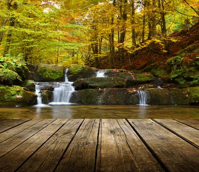 Empty wooden deck table with autumn waterfall background. Ready for product display montage. 