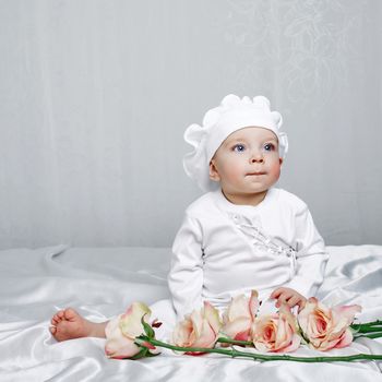 Little girl sitting on silk sheets lie at the feet of flowers