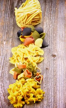 Stack of Spaghetti Nest, Pasta Shells, Bow Tie Pasta, Heart Shaped Pasta and Fusillini In a Row closeup on Rustic Wooden background