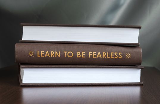 Books on a table and one with " Learn to be fearless. " cover. Book concept.