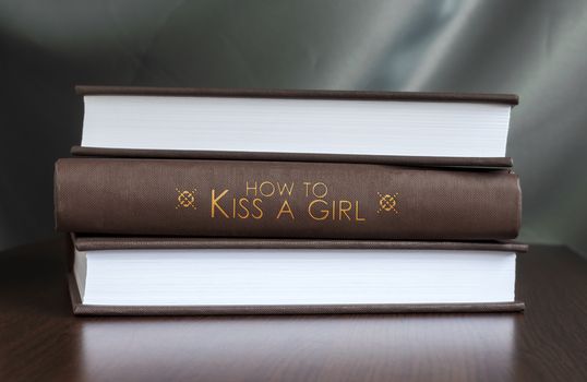 Books on a table and one with " How to kiss a girl " cover. Book concept.