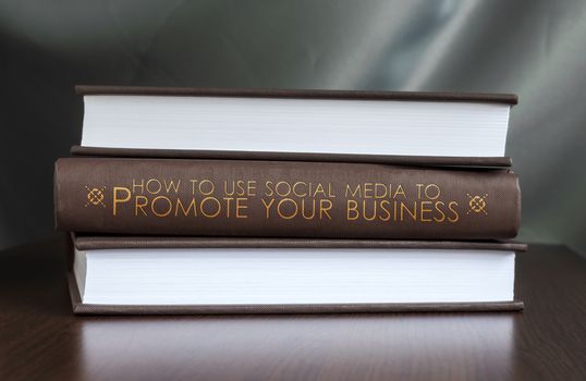 Books on a table and one with " How to use social media to promote your business " cover. Book concept.