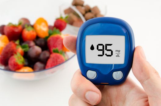 Hand holding meter. Diabetes doing glucose level test. Fruits in background