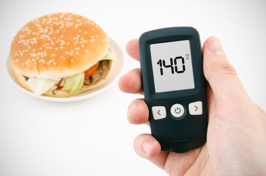Hand holding meter. Diabetes doing glucose level test. Hamburger in background