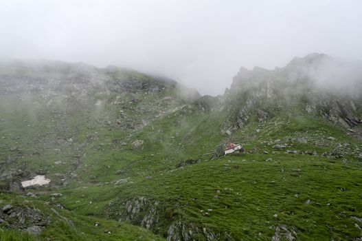 Morning mountain landscape with fog and a small building